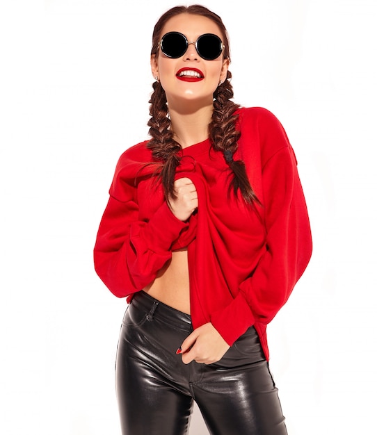 Porträt des jungen glücklichen lächelnden Frauenmodells mit hellem Make-up und den bunten Lippen mit zwei Zöpfen und Sonnenbrille in der roten Kleidung des Sommers lokalisiert.