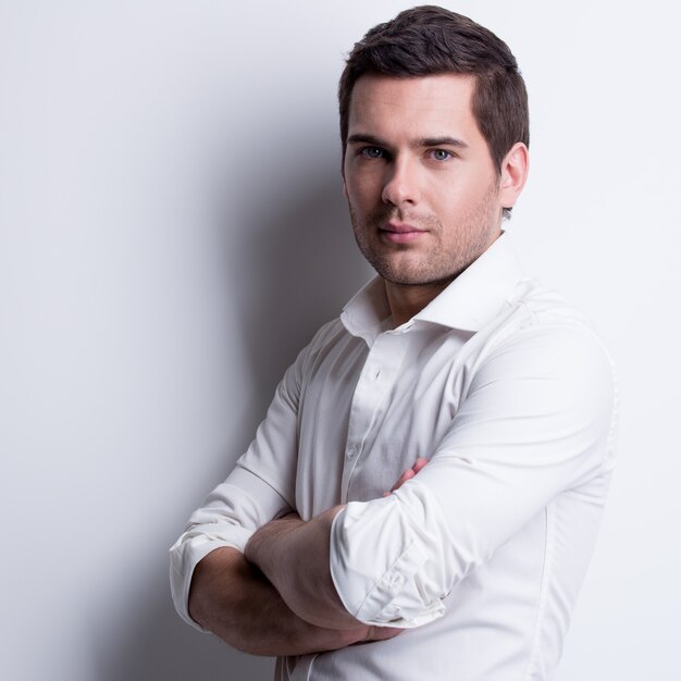 Porträt des jungen gutaussehenden Mannes im weißen Hemd wirft über Wand mit Kontrastschatten auf.