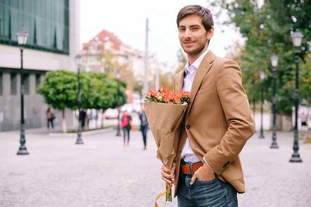 Porträt des jungen gutaussehenden Mannes lächelnd, der einen Strauß Rosen hält