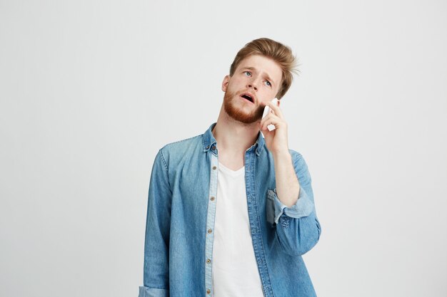 Porträt des jungen gutaussehenden Mannes mit Bart, der am Telefon spricht.