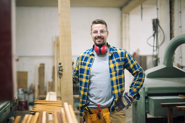 Porträt des jungen Holzarbeiters, der Holz in seiner Tischlerei hält