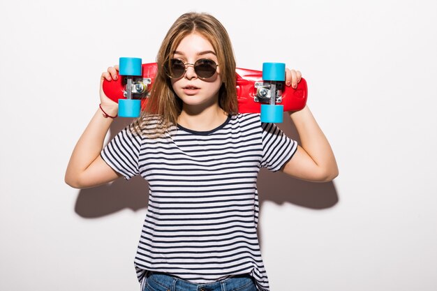 Porträt des jungen jugendlich Mädchens in der Sonnenbrille, die mit Skateboard beim Stehen über weißer Wand aufwirft