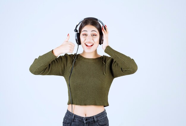 Porträt des jungen Mädchens in den Kopfhörern, die Musik hören und Daumen aufgeben.