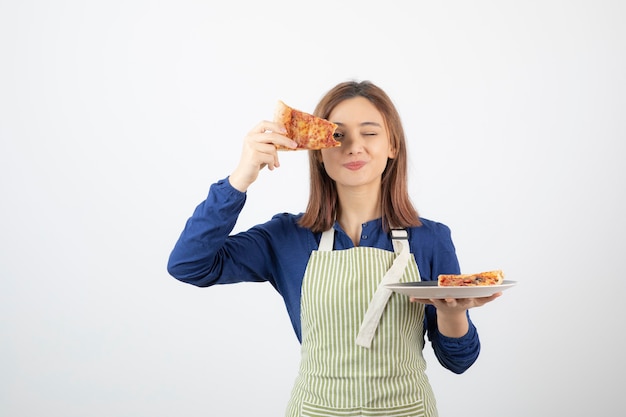 Porträt des jungen Mädchens in der Schürze, die Pizza auf Weiß zeigt