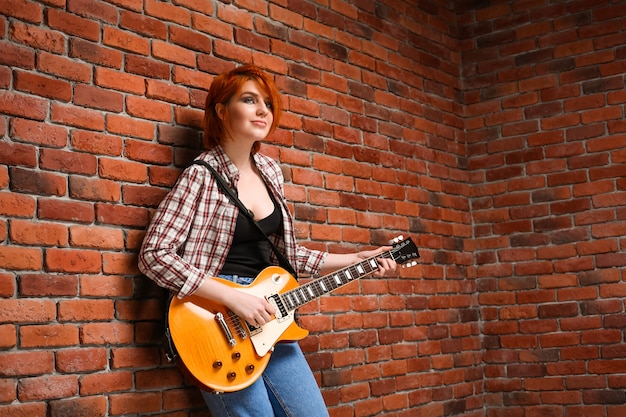 Porträt des jungen Mädchens mit Gitarre über Backsteinhintergrund.