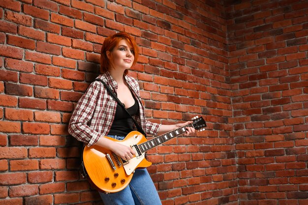 Porträt des jungen Mädchens mit Gitarre über Backsteinhintergrund.