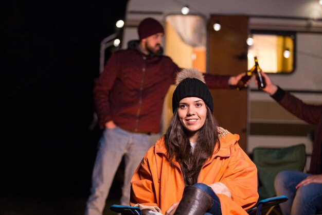 Porträt des jungen Mädchens vor Retro-Wohnmobil mit Freunden, die im Hintergrund Bier klirren.