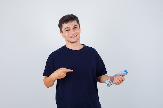 Porträt des jungen Mannes, der auf Flasche Wasser im schwarzen T-Shirt zeigt und zuversichtliche Vorderansicht schaut