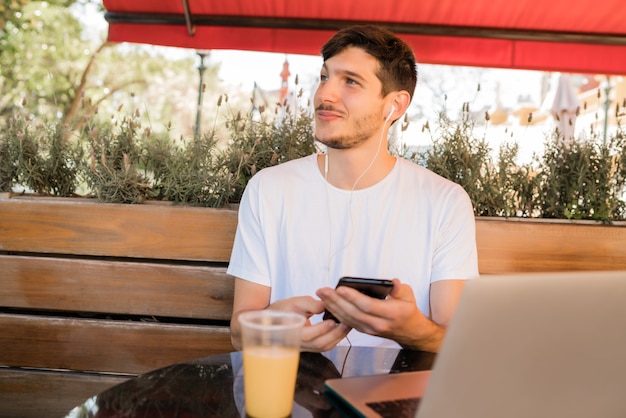 Porträt des jungen Mannes, der Handy beim Sitzen in einem Kaffeehaus im Freien verwendet. Kommunikationskonzept.