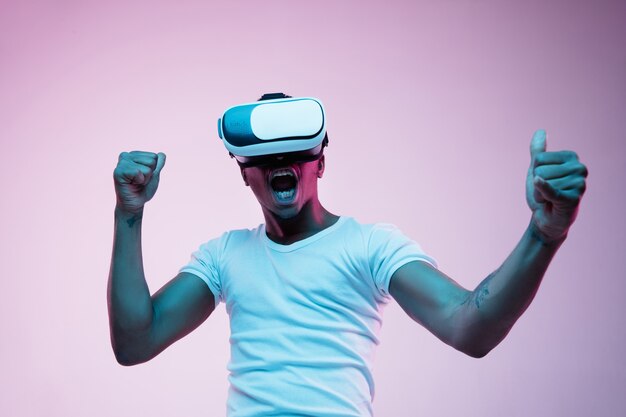 Porträt des jungen Mannes, der in VR-Brille im Neonlicht spielt