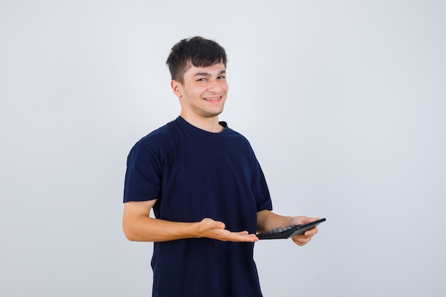 Porträt des jungen Mannes, der Rechner im schwarzen T-Shirt hält und fröhliche Vorderansicht schaut
