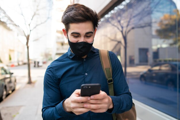 Porträt des jungen Mannes, der sein Handy benutzt, während man draußen auf der Straße geht. Neues normales Lifestyle-Konzept. Stadtkonzept.