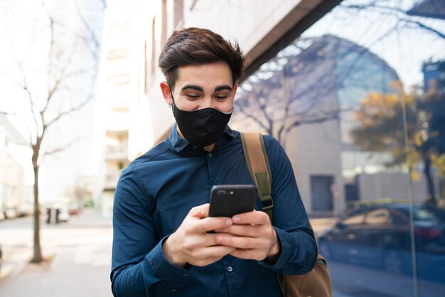 Porträt des jungen Mannes, der sein Handy benutzt, während man draußen auf der Straße geht