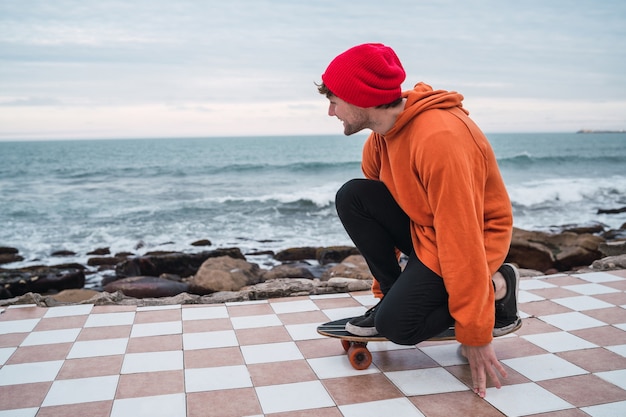 Porträt des jungen mannes, der spaß mit seinem skateboard hat und seine tricks mit meer im raum übt.