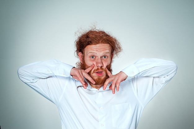 Kostenloses Foto porträt des jungen mannes mit langen roten haaren und mit schockiertem gesichtsausdruck auf grauem hintergrund