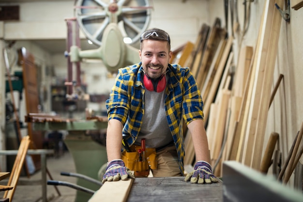 Porträt des jungen motivierten Zimmermanns, der an der Holzbearbeitungsmaschine in seiner Tischlerwerkstatt steht