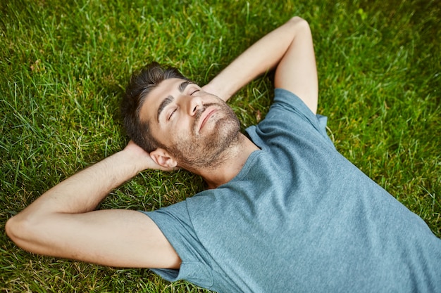 Porträt des jungen reifen gutaussehenden kaukasischen Mannes im blauen Hemd friedlich liegend auf Gras mit ja geschlossen.