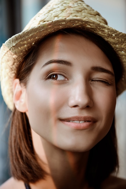 Porträt des jungen schönen brünetten Mädchens im Hut lächelnd, zwinkernd.