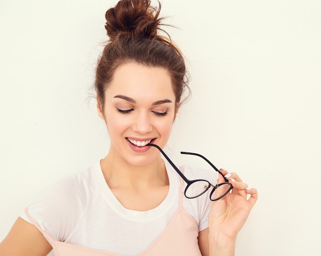 Porträt des jungen schönen Brunettefrauen-Mädchenmodells mit nacktem Make-up im bunten Sommerrosahippie kleidet die Aufstellung nahe Wand. Brille beißen