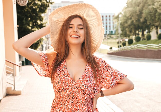 Porträt des jungen schönen lächelnden Hipster-Mädchens im trendigen Sommer-Sommerkleid. Sexy sorglose Frau, die auf dem Straßenhintergrund im Hut bei Sonnenuntergang aufwirft. Positives Modell im Freien