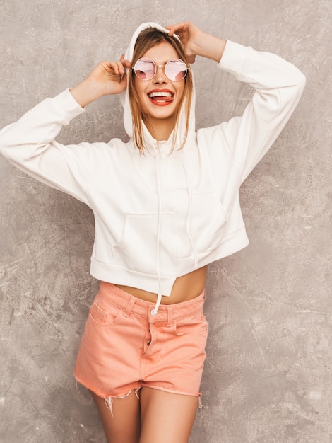 Porträt des jungen schönen lächelnden Mädchens im modischen Sommersport kleidet. Sexy sorglose Frauenaufstellung. Positives Modell, das Spaß in der Sonnenbrille hat