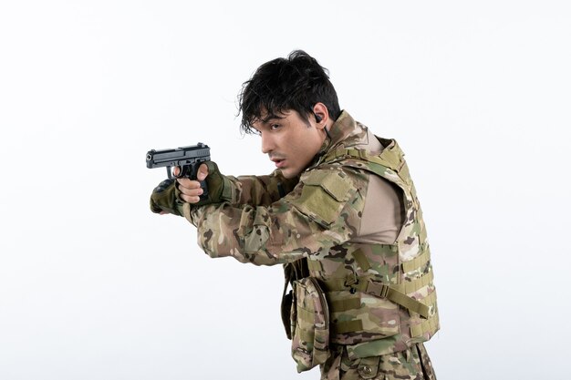 Porträt des jungen Soldaten in Tarnung mit Gewehr auf weißer Wand