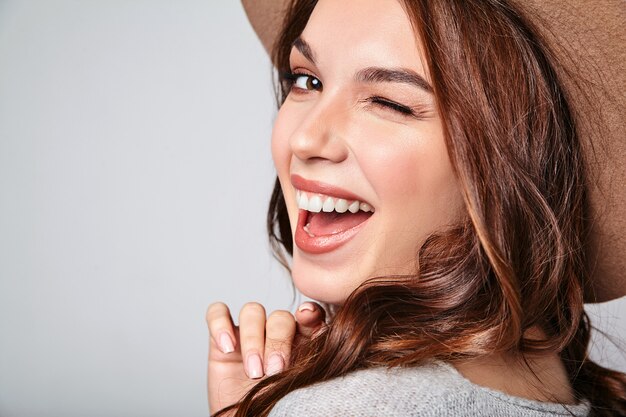 Porträt des jungen stilvollen lachenden Modells in der grauen lässigen Sommerkleidung im braunen Hut mit natürlichem Make-up