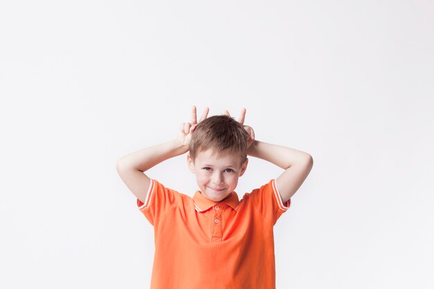 Porträt des Jungenkindes Finger hinter seinem Kopf zeigend und gegen weißen Hintergrund neckend