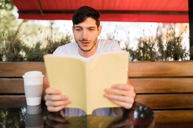 Porträt des kaukasischen Mannes, der Freizeit genießt und ein Buch liest, während draußen im Café gesessen wird. Lifestyle-Konzept.