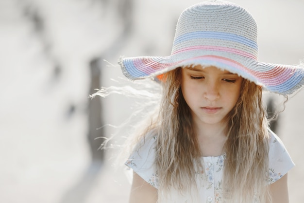 Porträt des kleinen blonden kaukasischen Mädchens im Hut mit traurigem Anblick