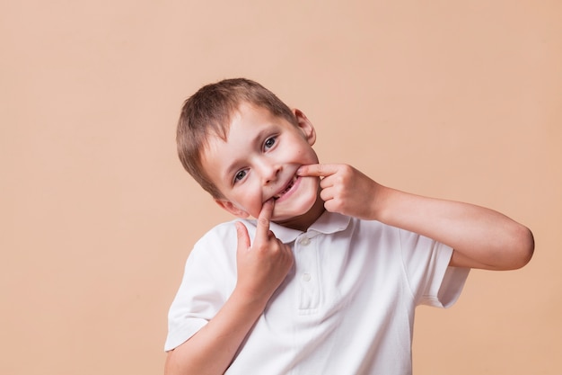 Porträt des kleinen Jungen Kamera betrachtend und auf beige Hintergrund neckend