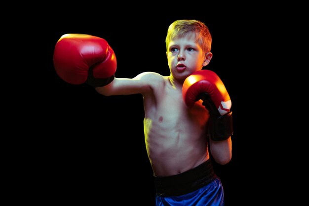 Porträt des kleinen Jungen Kindertrainingsboxen isoliert über schwarzem Studiohintergrund in Neonlicht Aktive Kindheit