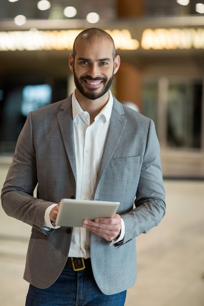 Porträt des lächelnden Geschäftsmannes unter Verwendung der digitalen Tablette im Wartebereich