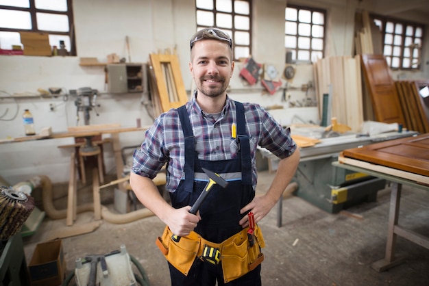 Porträt des lächelnden gutaussehenden Handwerkers, der Hammer in seiner Werkstatt hält