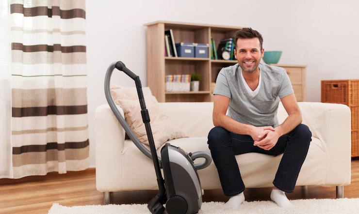 Kostenlose Foto porträt des lächelnden mannes mit staubsauger im wohnzimmer