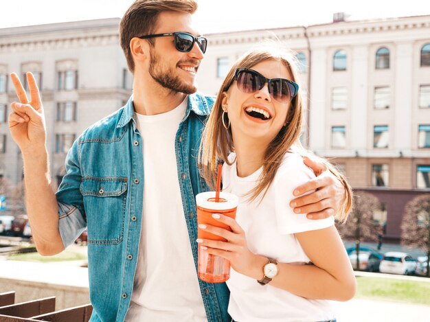 Porträt des lächelnden schönen Mädchens und ihres hübschen Freundes in der zufälligen Sommerkleidung. . Mit einer Flasche Wasser und Strohhalm