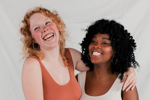Porträt des Lächelns von zwei multi ethnischen Freundinnen gegen grauen Hintergrund