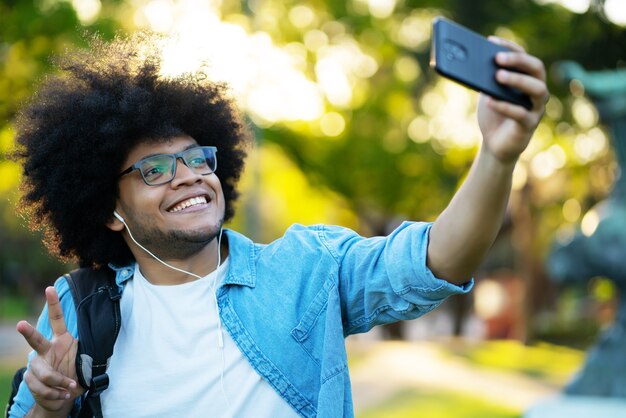 Porträt des lateinischen Mannes, der ein Selfie mit seinem Handy nimmt, während draußen auf der Straße stehend