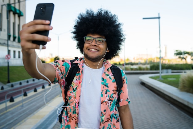 Porträt des lateinischen Mannes, der ein Selfie mit seinem Handy nimmt, während draußen auf der Straße stehend