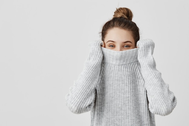 Porträt des Mädchens, das ihren trendigen Pullover über Kopf zieht, der Spaß hat. Frau mit gebundenem Haar im Haarknoten, der kindisch ist und in ihren Kleidern verschwindet, die von unten schauen. Glückskonzept