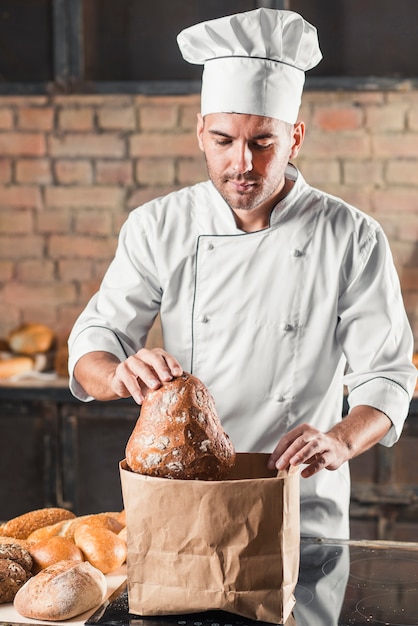 Porträt des männlichen Bäckers Brotlaib von der Papiertüte halten