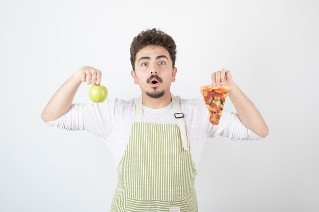 Porträt des männlichen Kochs, der Pizza und grünen Apfel auf Weiß hält