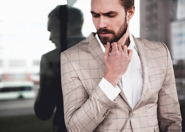 Kostenloses Foto porträt des männlichen vorbildlichen mannes der sexy hübschen mode kleidete im eleganten beige karierten anzug an, der auf dem straßenhintergrund aufwirft