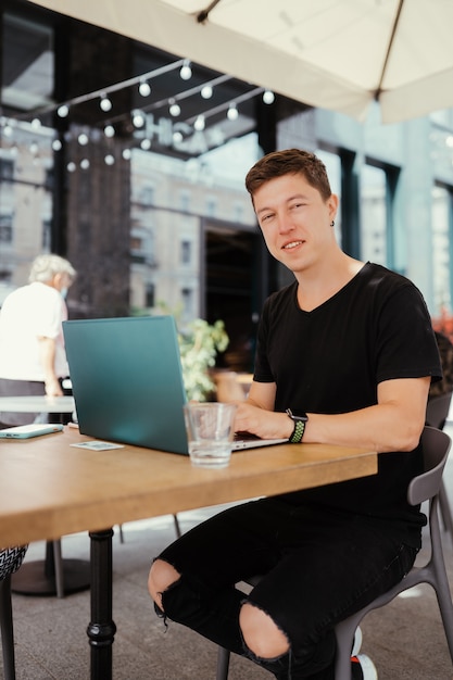 Porträt des Mannes, der an einem Tisch sitzt, der an einem Laptop arbeitet.