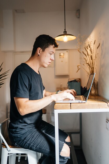 Porträt des Mannes, der an einem Tisch zu Hause sitzt und an einem Laptop arbeitet.