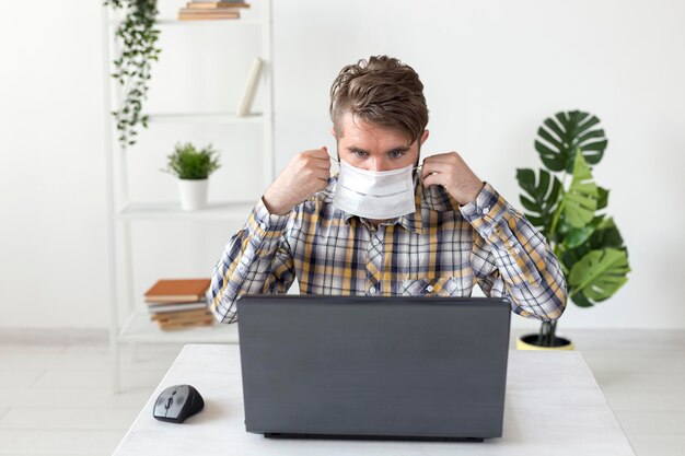 Porträt des Mannes mit Gesichtsmaske, die auf Laptop arbeitet