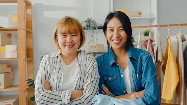 Porträt des Modedesigners der jungen asiatischen Frauen mit glücklichem Lächeln, verschränkten Armen und Blick nach vorne beim Arbeiten des Bekleidungsgeschäfts im Heimbüro