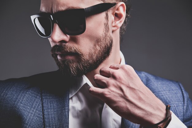 Porträt des modischen Hipster-Geschäftsmannmodells der schönen Mode, gekleidet im eleganten blauen Anzug auf Grau