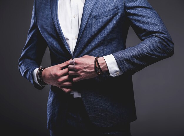 Porträt des modischen Hipster-Geschäftsmannmodells der schönen Mode, gekleidet im eleganten blauen Anzug, der auf Grau aufwirft