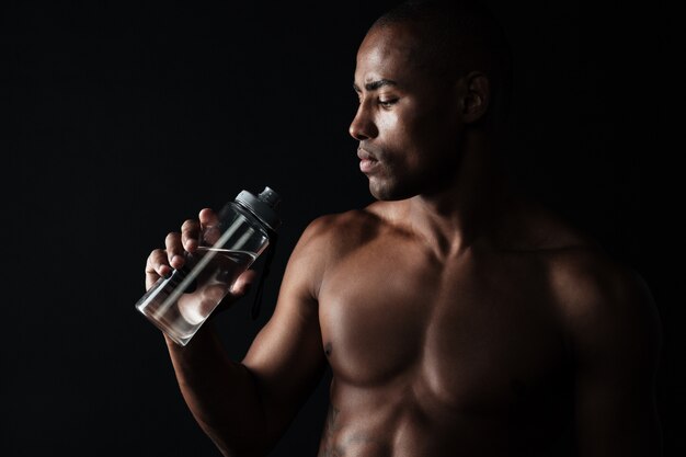 Porträt des müden jungen afroamerikanischen Sportmannes, der Flasche Wasser hält